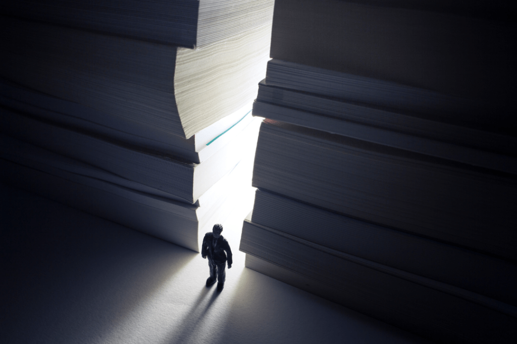 A graphic of a person standing between giant stacks of paper.