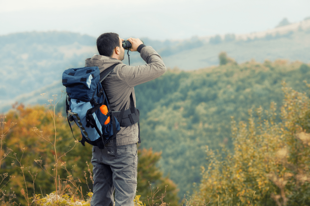 Male hiker looking through binoculars at a hilly landscape