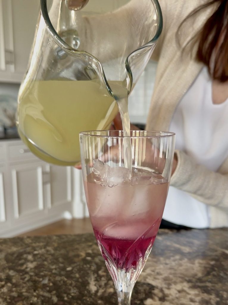 Close up of pouring lemon juice into a glass with ice and butter pea flower tea-infused simple syrup.