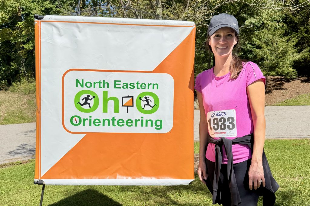 A woman standing by a larger sign that says Northeastern Ohio Orienteering.